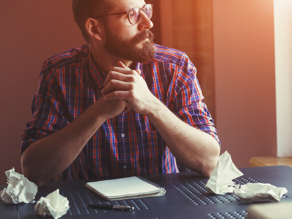 Bearded man sitting near blank copy book and thinking,