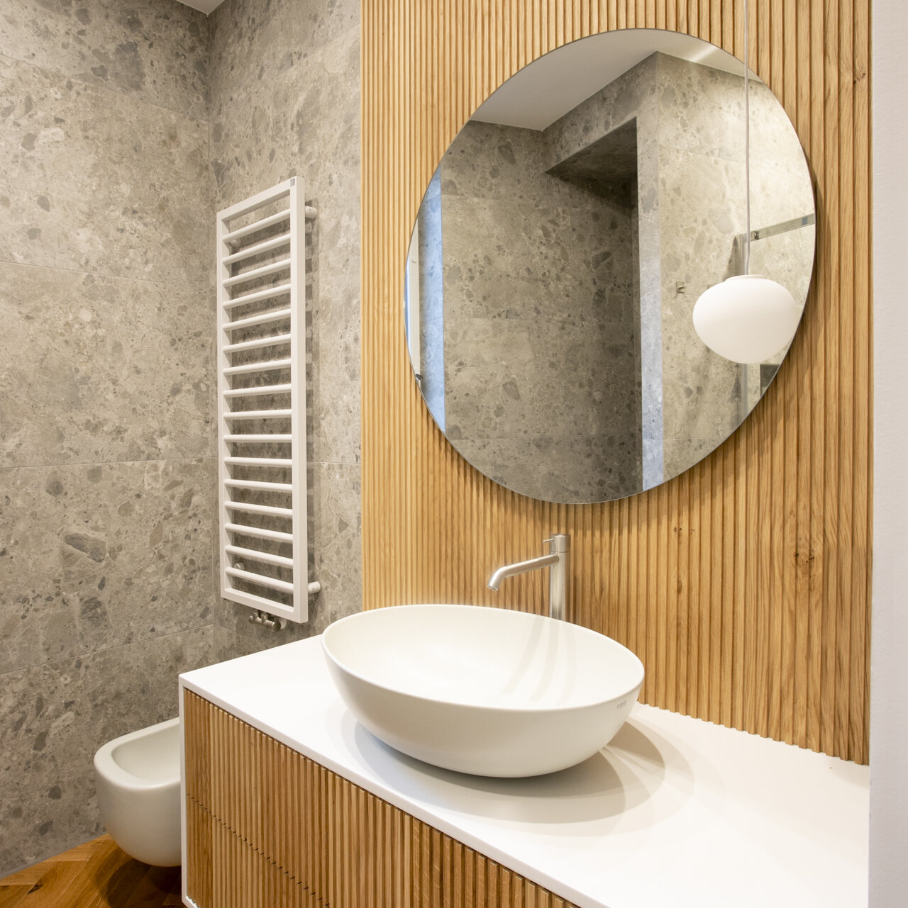 Un bagno con pareti effetto pietra e un mobile in legno a completare un radiatore in colore bianco opaco posizionato sulla parete